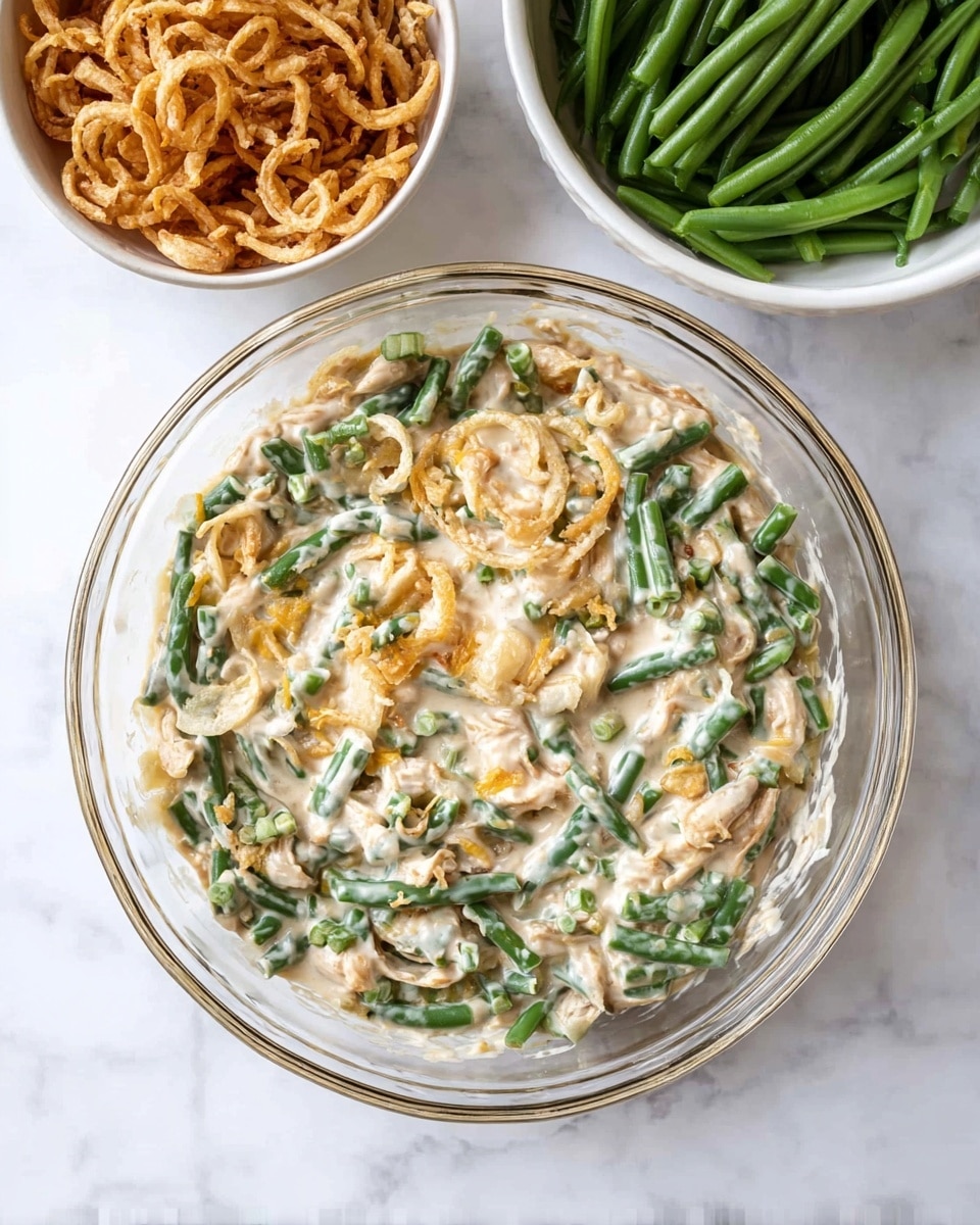 A clear glass bowl filled with a creamy green bean casserole sits at the center, showing a mix of chopped green beans covered in a thick, light beige sauce with some pale yellow melted cheese bits throughout. To the upper right, a white bowl holds bright green fresh green beans, and to the upper left, a smaller white bowl contains crispy fried onion rings in a light golden brown color. All bowls rest on a white marbled surface, creating a clean and fresh look. Photo taken with an iphone --ar 4:5 --v 7