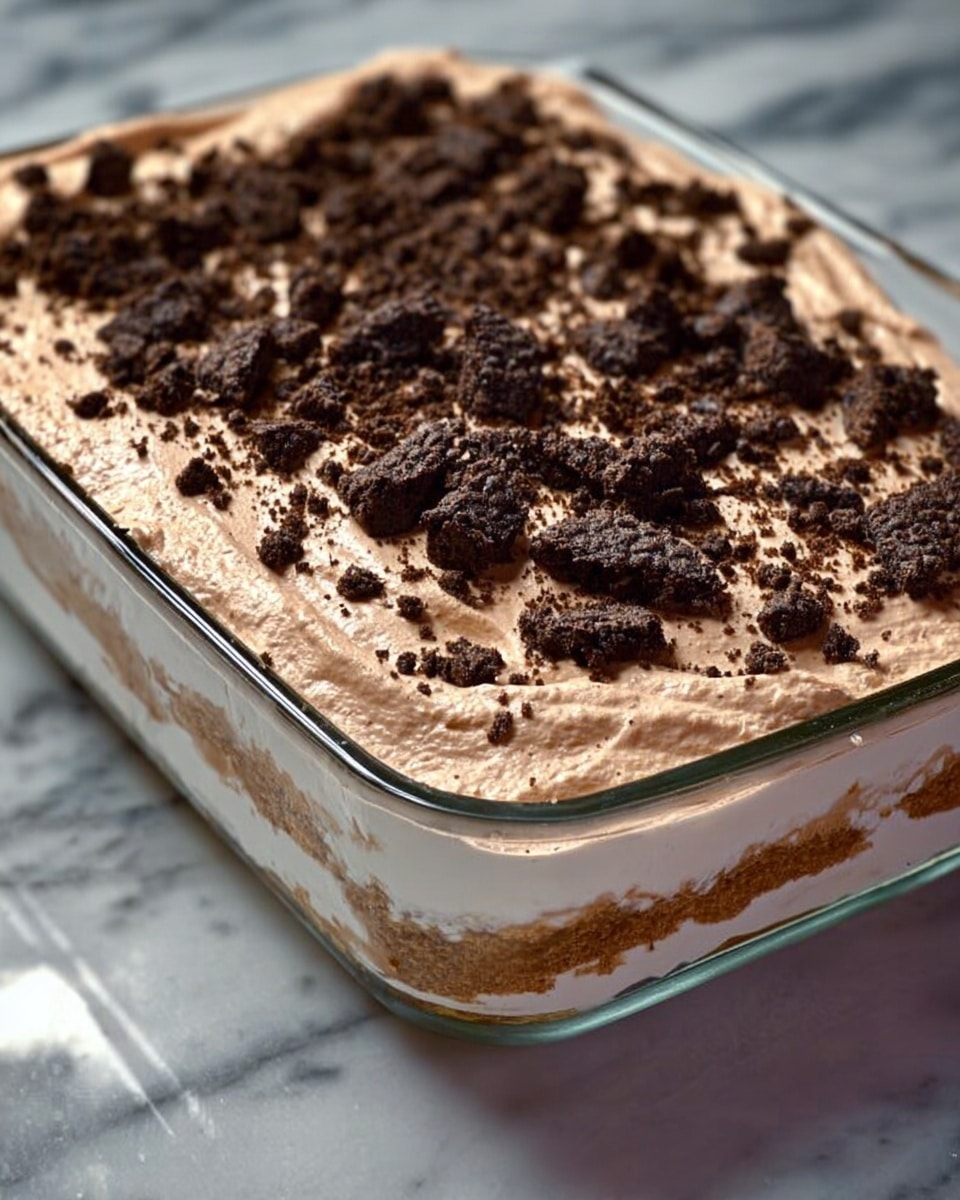 The image shows a clear glass rectangular dish filled with a layered dessert. The bottom layer is thick and creamy white. The middle layer is light brown and smooth, covering the first layer evenly. The top layer is more fluffy and lighter brown, spread evenly with many dark brown crushed cookie pieces scattered on it. The dish sits on a white marbled surface, and the lighting highlights the creamy and textured layers inside the dish. photo taken with an iphone --ar 4:5 --v 7