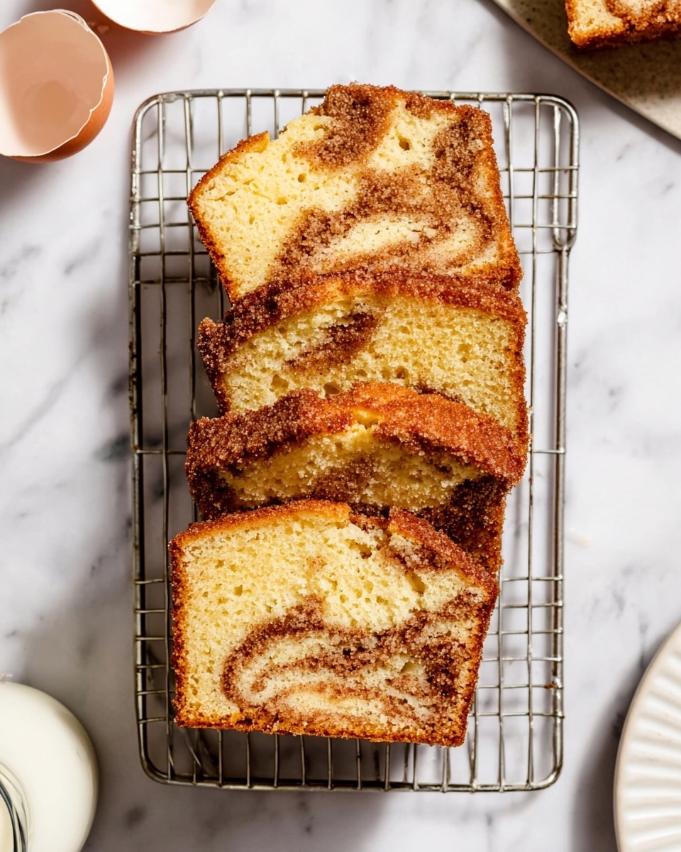 Four slices of cinnamon sugar loaf cake are stacked on a metal cooling rack, placed on a white marbled surface. Each slice shows a light yellow, soft crumb with swirls of darker cinnamon brown inside. The top of each slice is coated with a crunchy cinnamon sugar layer, giving a slightly rough texture and a deep brown color. The edges are golden brown and slightly crispy. On the left side, there is an eggshell half visible, and at the bottom left corner, part of a small white jug filled with milk can be seen. A partial view of the same cake on a white plate is visible on the right edge of the image. photo taken with an iphone --ar 4:5 --v 7