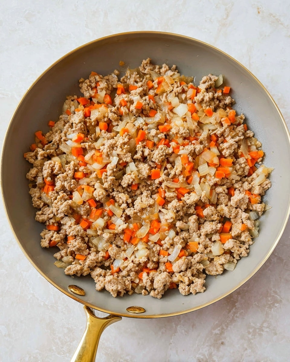 A light gray pan with a shiny golden handle is filled with cooked ground meat mixed with small pieces of white onion and bright orange carrot. The meat looks soft and crumbly, spreading evenly across the pan. The onions are translucent and cut into small chunks, while the carrots add bright spots of color throughout. The pan sits on a white marbled surface. photo taken with an iphone --ar 4:5 --v 7
