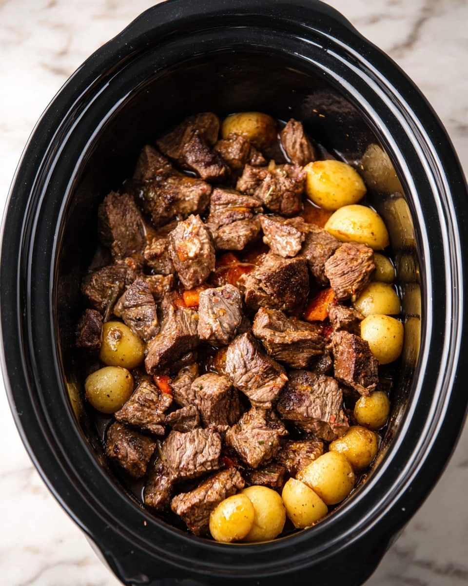 An oval black slow cooker filled with a layer of small yellow round potatoes at the bottom, covered by a thick layer of browned beef chunks showing a mix of brown grilled edges and some pink inner parts, creating a rough textured and hearty look, all placed on a white marbled surface photo taken with an iphone --ar 4:5 --v 7