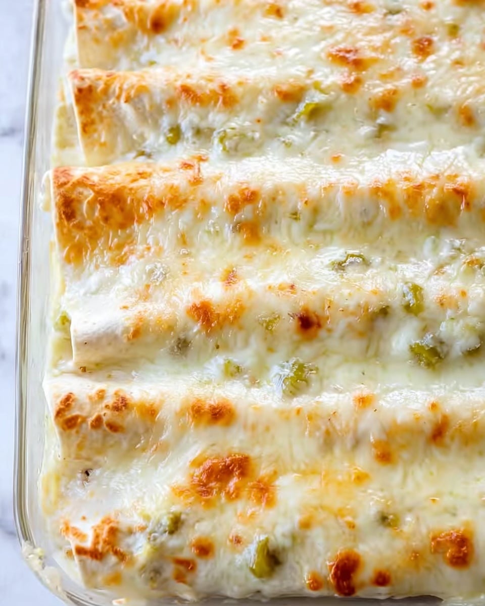 A close-up view of three rolled enchiladas placed side by side in a clear glass baking dish on a white marbled surface. Each enchilada is covered with a smooth, melted cheese layer that is golden brown in spots, showing a slightly bubbly texture. Beneath the cheese layer, small pieces of green chili peppers are visible, peeking through the creamy sauce that lightly coats the tortillas, giving a soft off-white appearance with hints of green. The dish displays a rich and creamy texture, highlighting the melted cheese's stretchiness and the peppers' subtle presence. Photo taken with an iphone --ar 4:5 --v 7