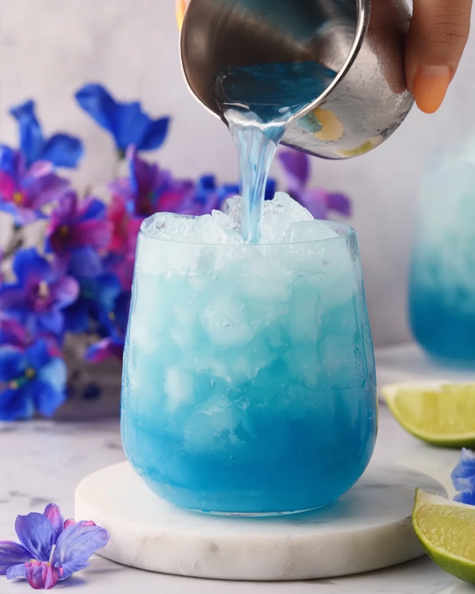 A white, uniquely shaped glass filled with a bright blue drink and ice cubes on top of a white marbled surface. A woman's hand is pouring more of the blue liquid from a small metallic cup into the glass, and blue and purple flowers are visible in the blurred background, along with a small piece of lime to the right. The overall look is fresh and colorful, emphasizing the bright blue drink. photo taken with an iphone --ar 4:5 --v 7