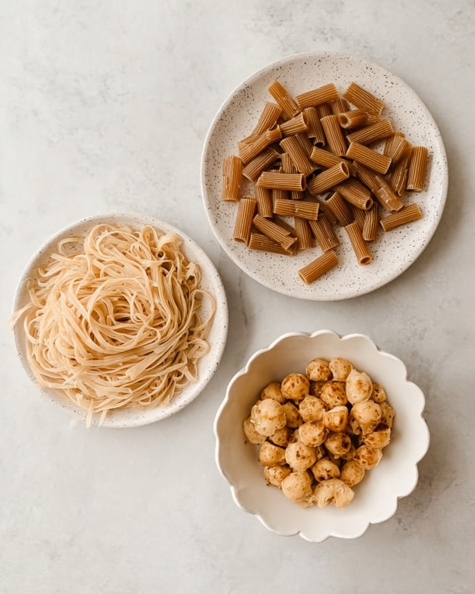 The image shows three white dishes on a white marbled surface. The top dish is a plain round plate filled with short brown pasta tubes, evenly spread out. The bottom left dish is a round plate with speckled details, holding a pile of thin, light beige noodles arranged loosely in a circular shape. The bottom right dish is a white bowl with a scalloped edge, filled with small, browned, round pieces that look like cooked bite-sized food, stacked closely together. photo taken with an iphone --ar 4:5 --v 7