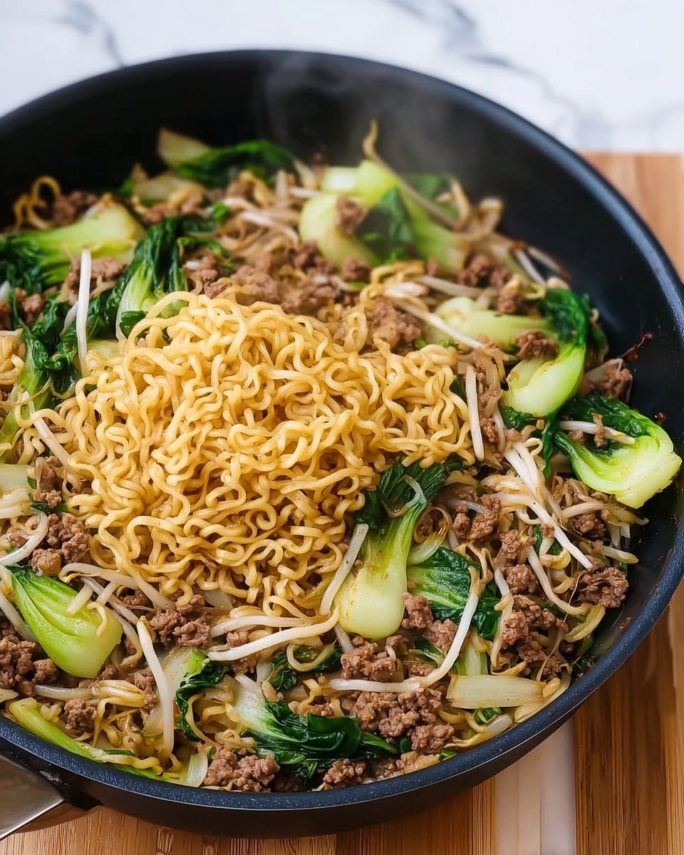The image shows a black pan full of cooked noodles mixed with browned ground meat, light green bok choy pieces, and white bean sprouts. The noodles are yellow and curly, sitting on top and in the middle of the pan. The ground meat is small, crumbly, and brown, mixed evenly with the noodles. The bok choy leaves are bright green with white stalks and are placed mostly around the edges, adding color contrast. Bean sprouts are scattered through the noodles, adding thin white strands. Slight steam rises from the dish, giving it a fresh cooked look. The pan is on a wooden surface with a white marbled background. photo taken with an iphone --ar 4:5 --v 7