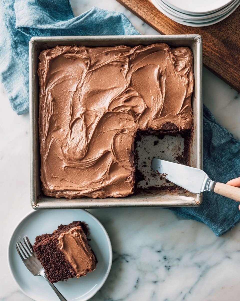 A square chocolate cake in a metal pan with thick, smooth milk chocolate frosting spread evenly on top, showing glossy swirls and soft texture; one piece is missing from the bottom left corner revealing a dark, moist chocolate cake layer beneath the frosting. Near the pan, a white plate holds the removed piece with the same two layers visible: a dark chocolate cake base and a thick milk chocolate frosting top. A fork rests on the plate, and a woman's hand holds a spatula digging into the pan. The scene is set on a white marbled surface with a folded blue cloth beside the pan and stacked white plates on a wooden board in the background. Photo taken with an iphone --ar 4:5 --v 7