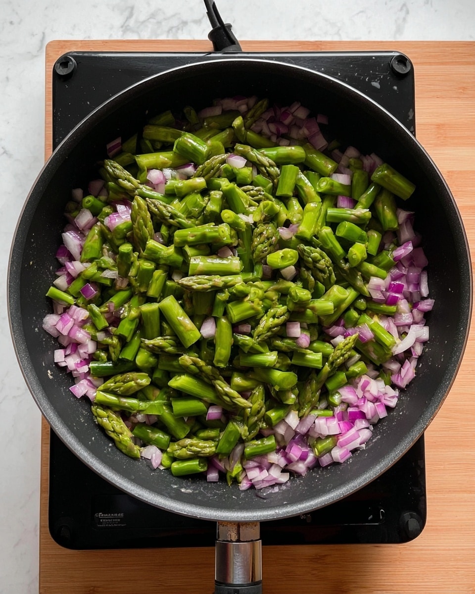 The image shows a black cooking pan on a black electric stove with a wooden countertop underneath. Inside the pan, there is one visible layer of chopped vegetables with two main colors: small pinkish-purple pieces of chopped onion spread evenly around the pan, and a thick layer of bright green chopped asparagus cut into short sections positioned on top of the onions. The green asparagus pieces have visible tips and stalks, adding texture and shape variety. The background surface is a white marbled texture. photo taken with an iphone --ar 4:5 --v 7