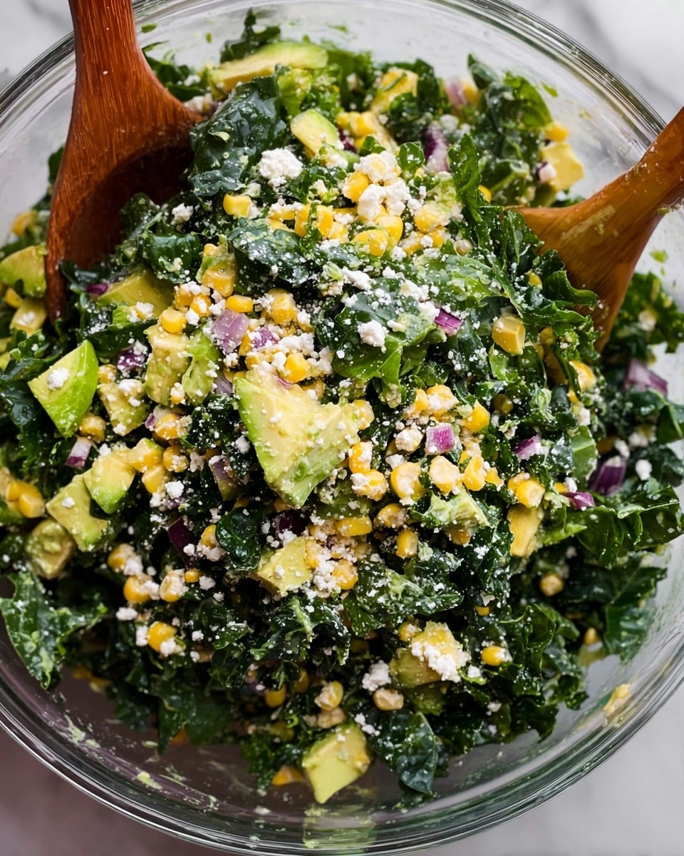 A large clear bowl is filled with a fresh salad showing three main layers: the bottom and biggest layer is dark green kale leaves with a rough texture, mixed with chunky yellow corn kernels and light green avocado pieces in the middle layer. Small white crumbles of cheese are sprinkled evenly on top, joined by tiny purple onion bits scattered throughout. Two wooden salad spoons are partly visible inside the bowl, mixing the salad. The bowl sits on a white marbled surface. Photo taken with an iphone --ar 4:5 --v 7