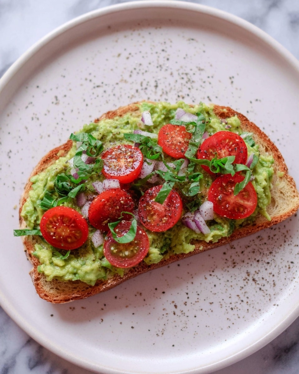 A single slice of toasted bread sits in the center of a white plate on a white marbled surface. The bread is topped with a thick layer of smashed green avocado spread evenly, followed by small cherry tomato halves that are bright red and juicy. Scattered chopped white onion pieces and fresh green basil leaves add contrast on top. There is a light sprinkle of black pepper dusted over the whole toast, adding a fine texture on the vibrant toppings. photo taken with an iphone --ar 4:5 --v 7