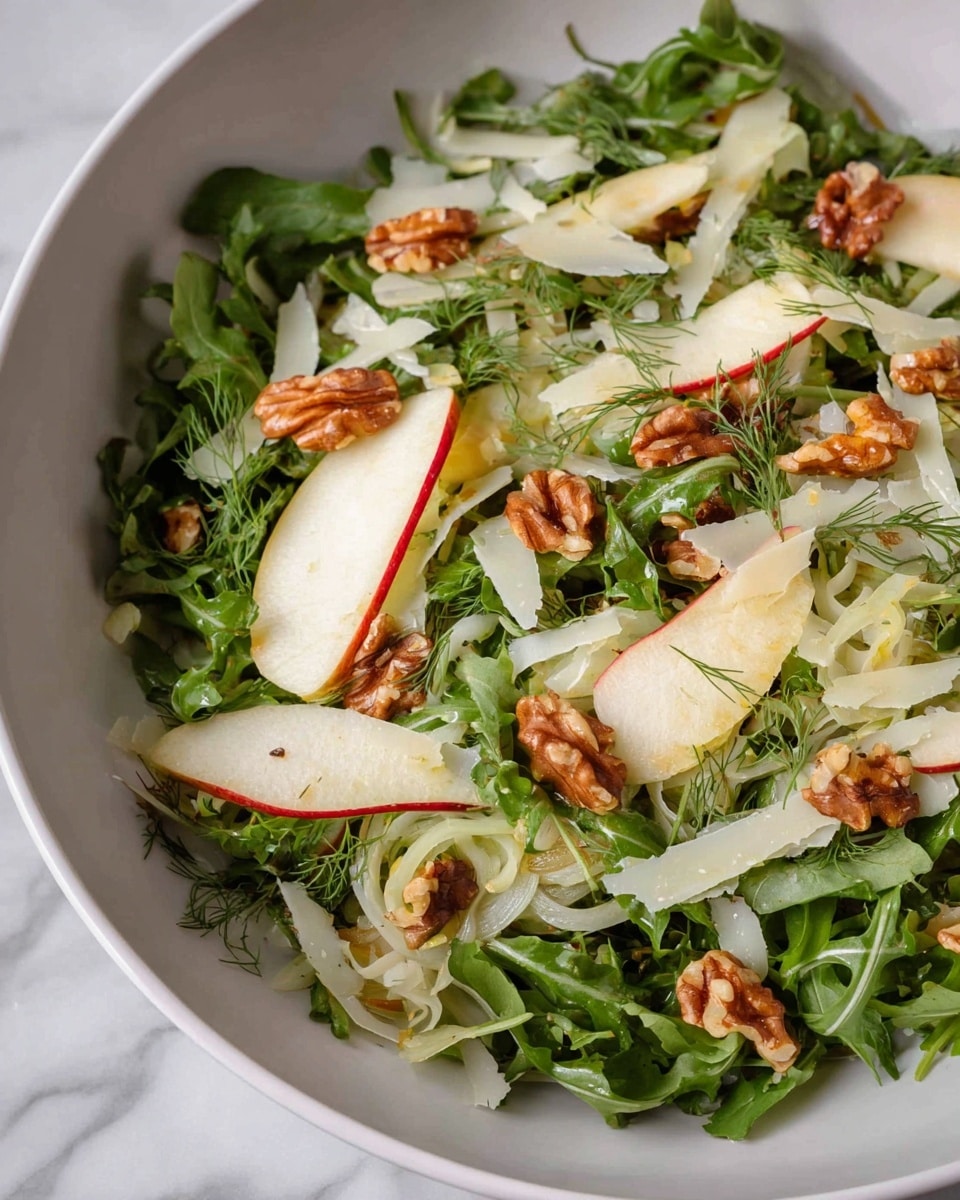 A fresh salad in a white bowl features a base layer of dark green leafy arugula. On top, there are thin pale rings of fennel and thin slices of white apple with red edges arranged evenly. Scattered walnut pieces add a warm brown color throughout. Thin strips of pale yellow cheese shavings are spread on top, and small bits of fresh green dill are sprinkled to add texture and contrast. The bowl sits on a white marbled surface. photo taken with an iphone --ar 4:5 --v 7