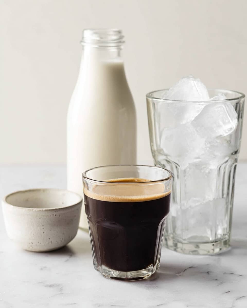 A small clear glass filled almost to the top with dark black coffee that has a thin layer of light brown foam on top sits in the front center. Behind the coffee glass to the right is a taller, clear glass filled with large, translucent ice cubes. To the left behind the coffee is a clear glass bottle filled about halfway with white milk. On the far left, there is a small white ceramic bowl with a rough texture. The items are set on a white marbled surface with a plain white background. photo taken with an iphone --ar 4:5 --v 7
