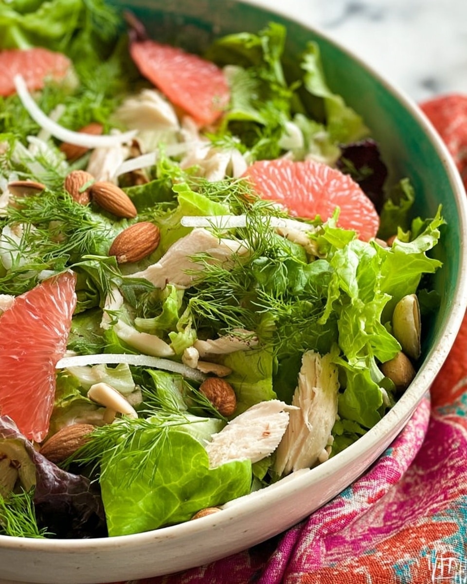 The image shows a fresh salad in a white bowl on a white marbled surface. The salad has many layers: at the bottom, there are mixed leafy greens in different shapes and shades of green. Scattered throughout are pink grapefruit segments, giving a bright contrast. Pieces of light-colored chicken are placed on top of the greens. Whole almonds are spread evenly over the salad, adding texture. Small dark dried berries or seeds are sprinkled carefully across the salad. Some delicate fennel fronds add a fine, feathery green layer to the top, making the salad look fresh and colorful. photo taken with an iphone --ar 4:5 --v 7