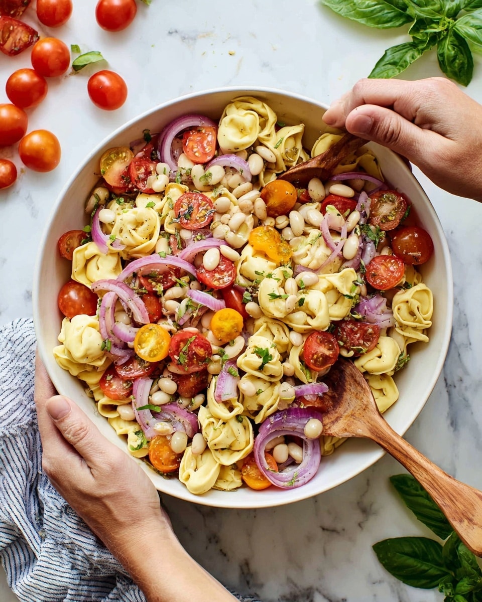 A large white bowl is filled with a colorful pasta salad made of three main layers: the bottom layer is light yellow tortellini pasta with soft, folded shapes, the middle layer contains small white beans scattered all over, and the top layer includes halved red and yellow cherry tomatoes along with thin, curved slices of purple onion. The ingredients are lightly mixed together and garnished with small green herb pieces. The bowl is held by two woman’s hands using wooden spoons, and the scene is set on a white marbled surface with extra cherry tomatoes and green basil leaves placed around it. photo taken with an iphone --ar 4:5 --v 7