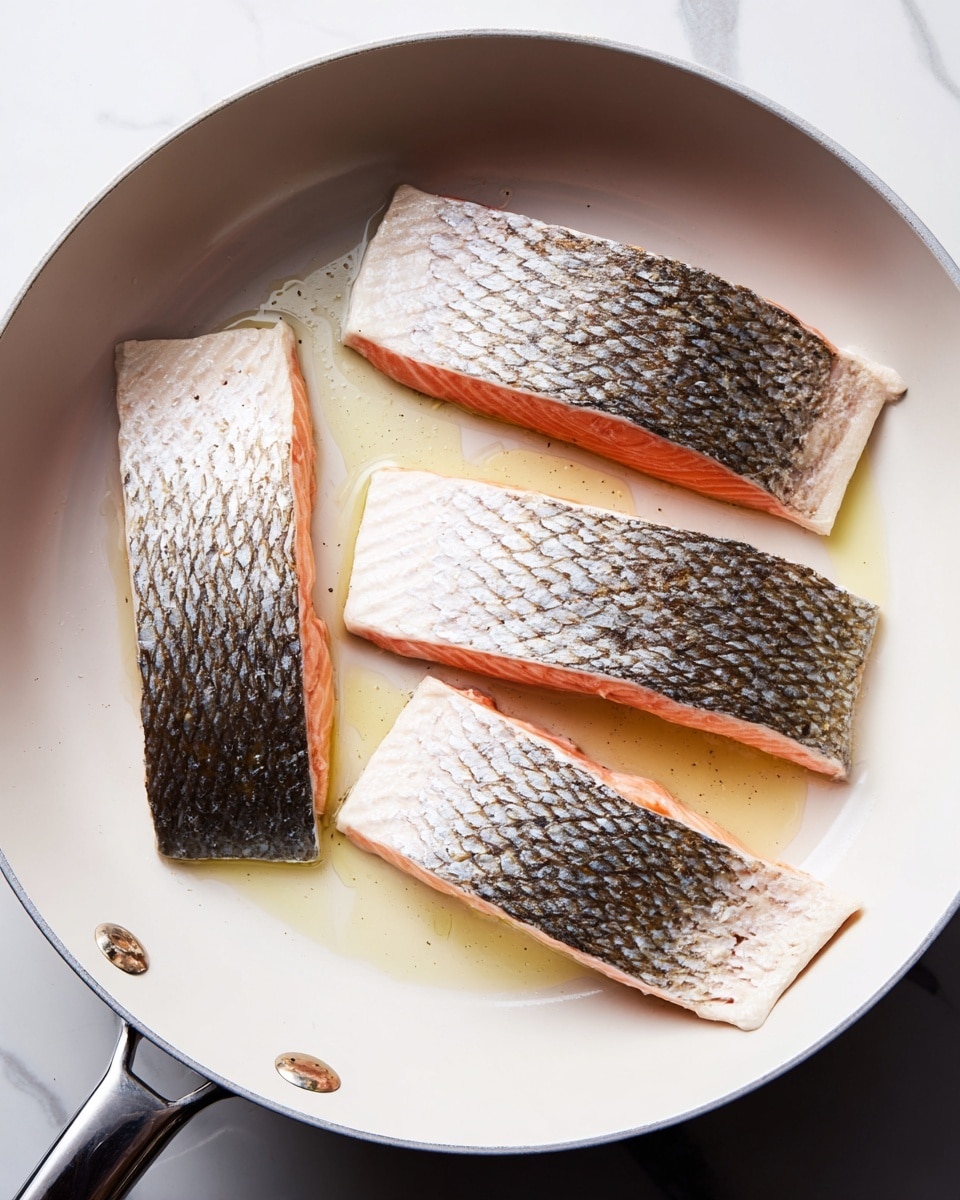 Four pieces of salmon with silvery, textured skin facing up are cooking in a white pan on a white marbled surface. The pink flesh is visible on the sides, and a light layer of oil shines beneath them. Three pieces are placed side by side near the top of the pan, while one piece is positioned horizontally near the bottom. The pan has a metal handle extending to the right. photo taken with an iphone --ar 4:5 --v 7
