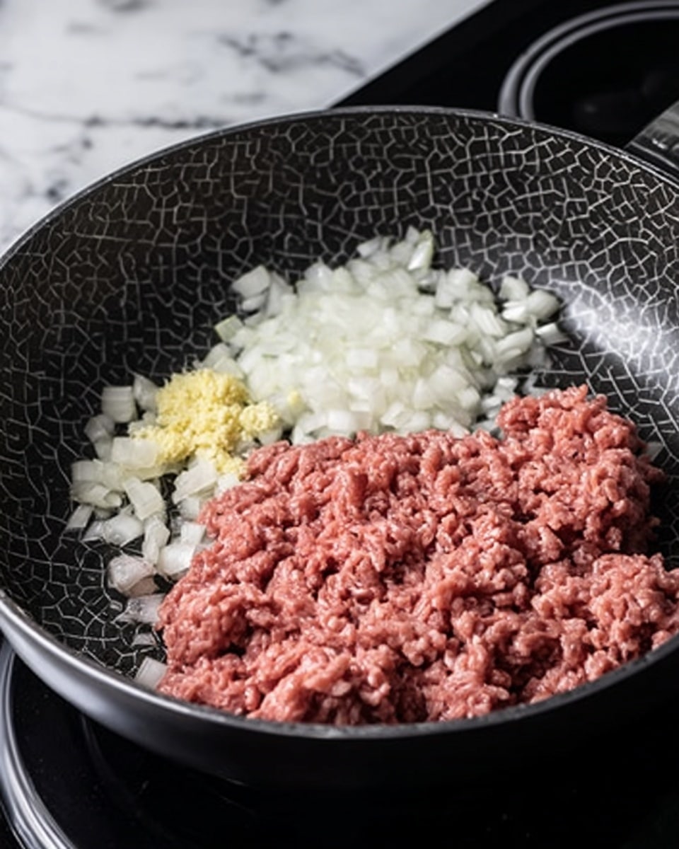 A close-up view of a non-stick frying pan on a stovetop, containing three main ingredients separate but close to each other: roughly half the pan filled with raw pink ground meat with a soft texture, a pile of finely chopped white onions with a translucent look on the right side, and a small mound of minced yellow garlic nestled between the meat and onions. The pan has a hexagonal patterned cooking surface and is placed on a black electric stove with round burners. The background and surface are a white marbled texture. Photo taken with an iphone --ar 4:5 --v 7