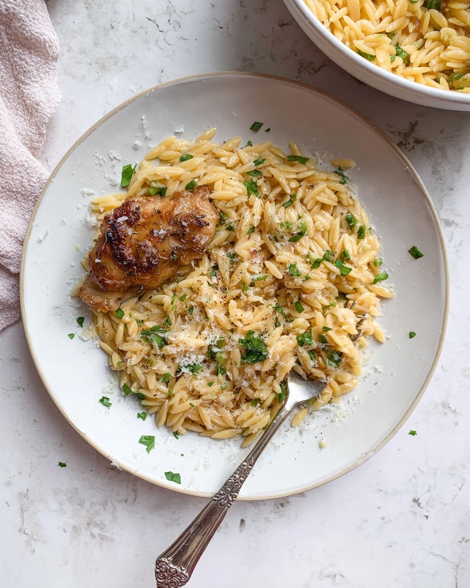 A white plate on a white marbled surface holds a serving of light golden brown orzo pasta mixed with small green parsley pieces, sprinkled lightly with grated cheese and black pepper. On the left side of the orzo sits a small piece of browned, cooked chicken with a slightly crispy skin. A silver fork rests on the right side of the plate, partially inserted into the orzo. The scene includes a white bowl in the top right corner filled with more orzo pasta. Photo taken with an iphone --ar 4:5 --v 7