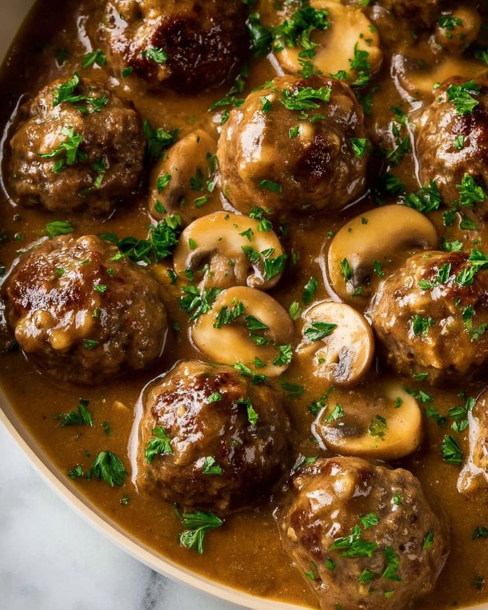A black cast iron pan filled with around twenty brown meatballs in a thick light brown sauce, scattered with light beige sliced mushrooms and small green herb bits on top, a metal spoon resting inside the pan. The pan is placed on a white marbled surface with a folded gray cloth near the top. Photo taken with an iphone --ar 4:5 --v 7
