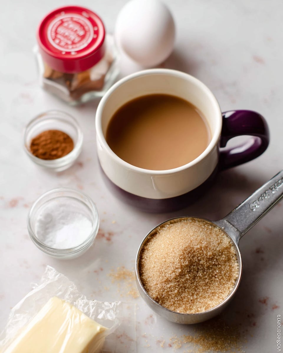 This image shows several baking ingredients placed on a white marbled surface. In the center, there is a white cup with a dark purple handle containing a light brown liquid. To the right, a metal measuring cup is filled with light brown sugar. Behind the cup, there is a white egg. On the left side, there is a small red-capped jar of ground cinnamon, a measuring cup filled with white liquid, and a small unwrapped stick of butter with a white wrapper. The items are spaced casually but clearly visible. Photo taken with an iphone --ar 4:5 --v 7