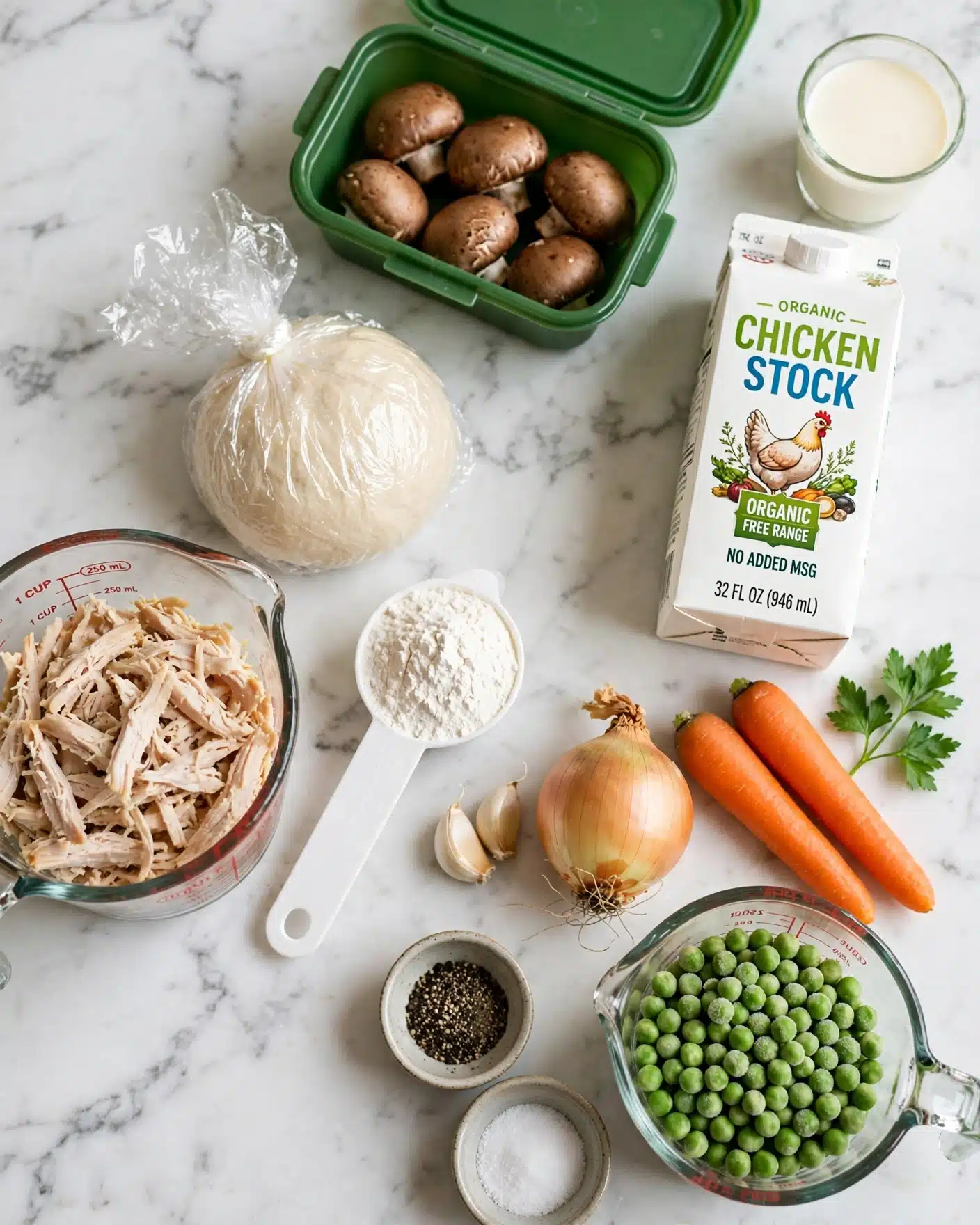The image shows ingredients for a dish placed neatly on a white marbled surface. There is a clear glass measuring cup filled with shredded cooked chicken on the left. Next to it is a white plastic measuring spoon with white flour. Above that is a round wrapped dough ball covered in clear plastic wrap. A green plastic container holds whole brown mushrooms in the top center. To the right is a white carton of organic chicken stock with colorful pictures and text. Below the carton are two bright orange carrots, a yellow onion with its roots still attached, and two cloves of garlic. There’s also a sprig of fresh green parsley next to the carton. To the bottom right is a clear glass measuring cup filled with frozen green peas, and beside it are small bowls containing black pepper and white salt. A small glass cup with cream is placed near the top right corner. photo taken with an iphone --ar 4:5 --v 7